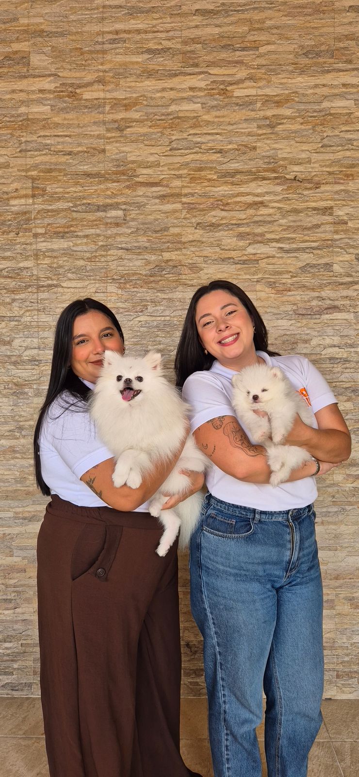 Duas veterinárias da NamuVet sorrindo e segurando cães Pomeranian brancos, demonstrando carinho e profissionalismo no atendimento domiciliar.